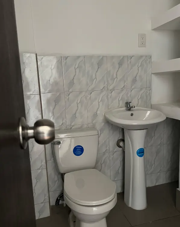 Baño terminado con azulejo tipo mármol, inodoro y lavamanos de pedestal