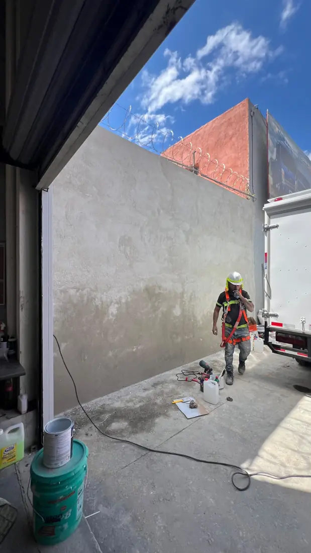 Operario con casco y arnés de seguridad preparando muro exterior para pintura