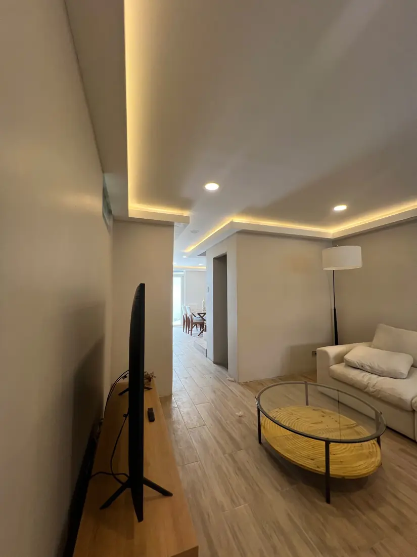Sala y pasillo con piso tipo madera y cielo falso iluminado