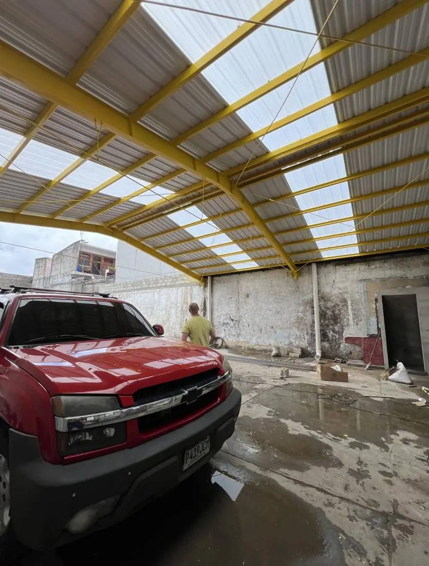 Estructura metálica amarilla con cubierta de lámina translúcida para parqueo
